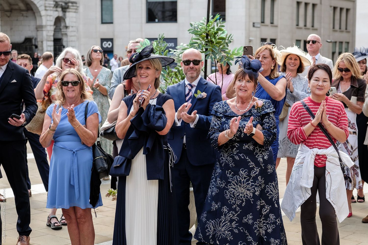 Guests clapping and smiling at an outdoor wedding celebration on a sunny day.