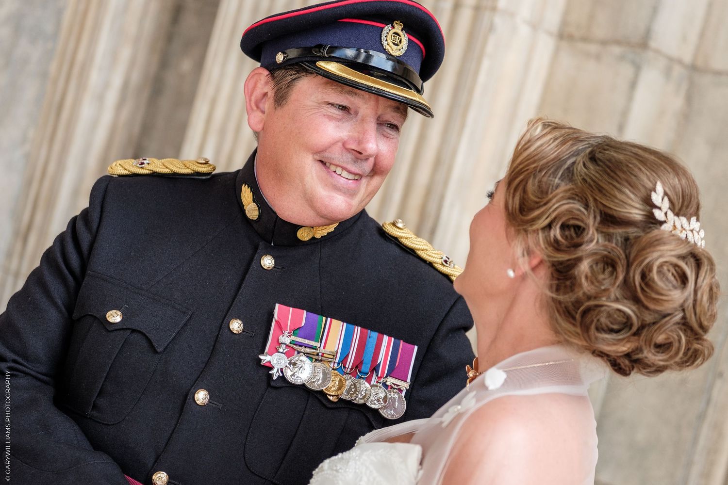 Military officer in uniform with medals smiles at bride in white dress during wedding ceremony.