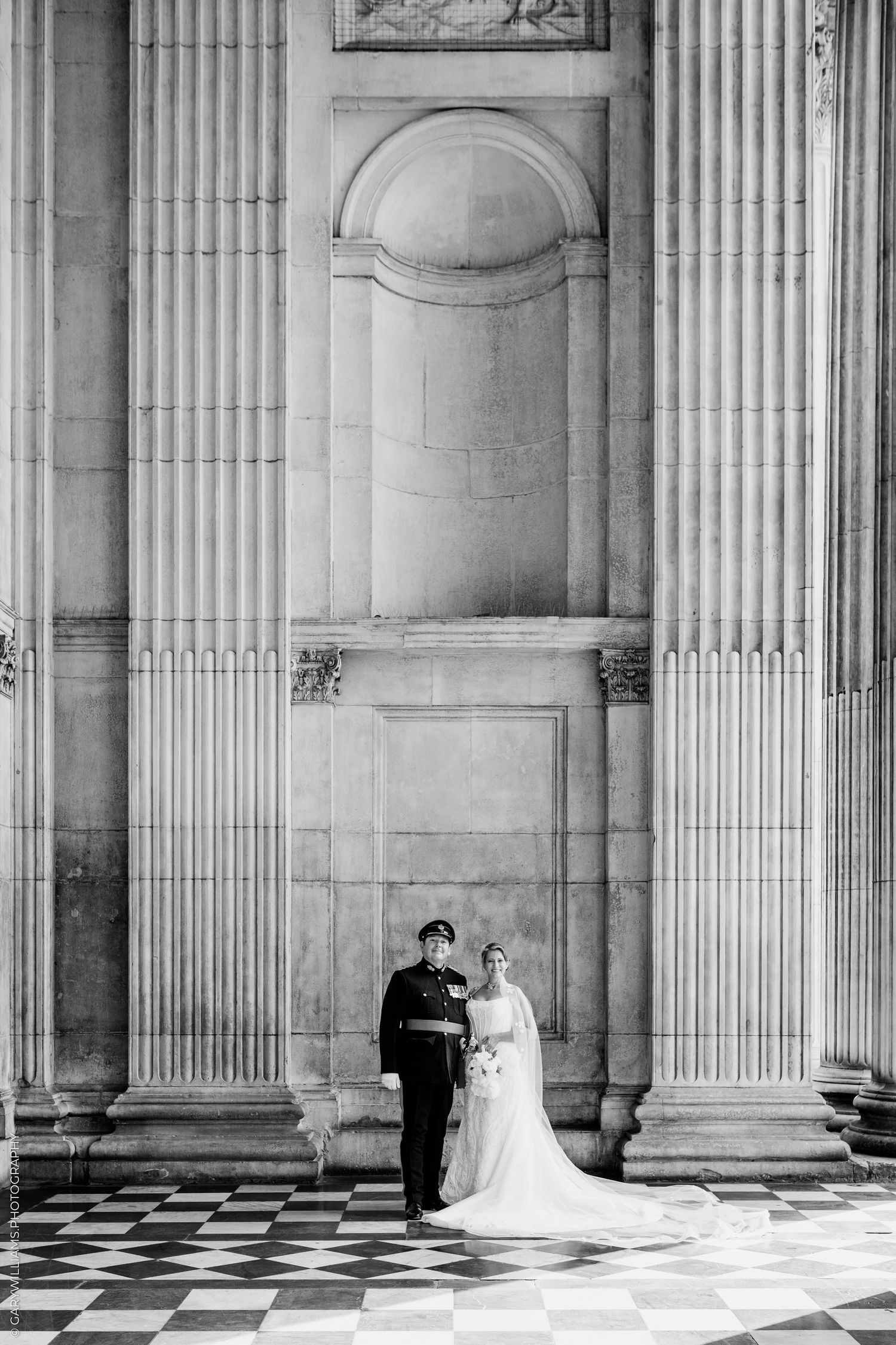 Black and white wedding photo of bride and groom standing between grand columns of a classical building.
