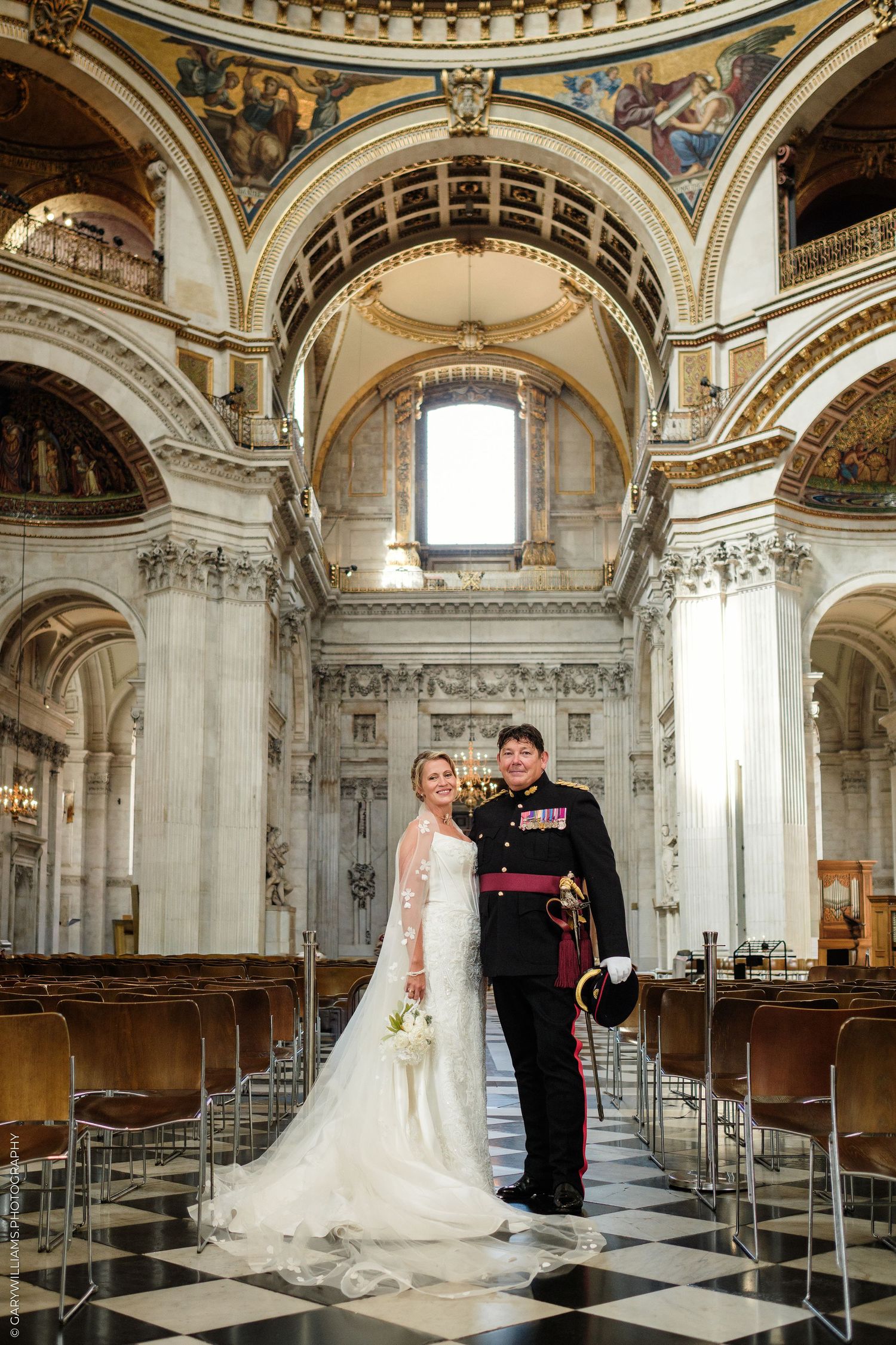 Bride and groom posing inside St. Paul's Cathedral London, bride in white gown, groom in military uniform.