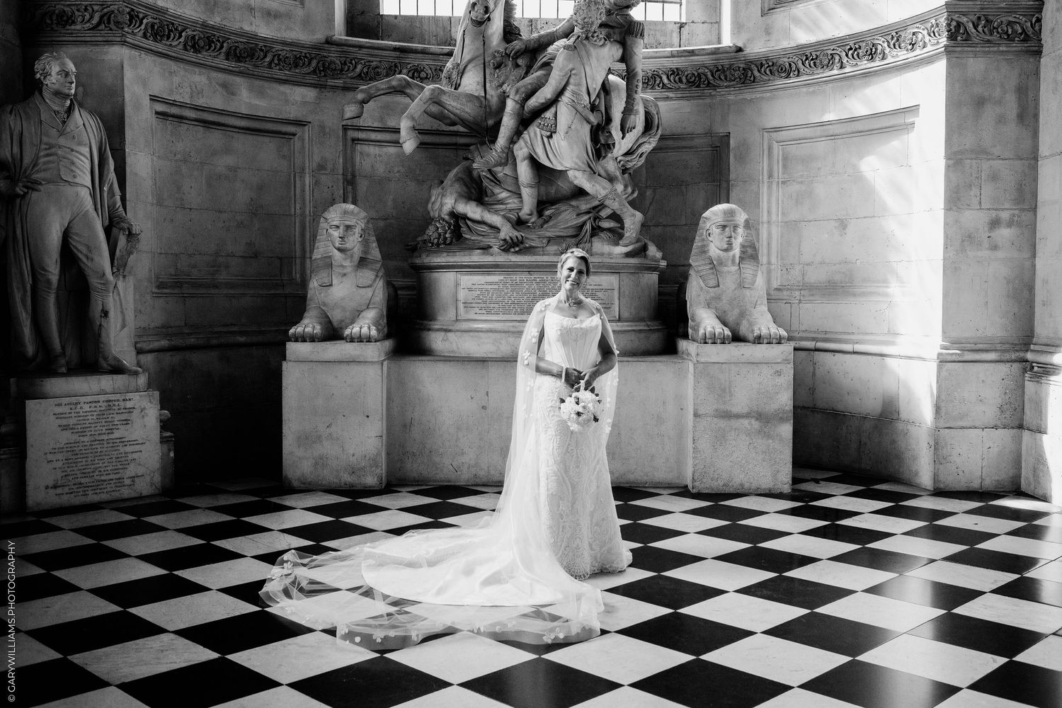 Black and white bridal portrait in ornate hall with checkered floor, sculptures, and dramatic lighting.