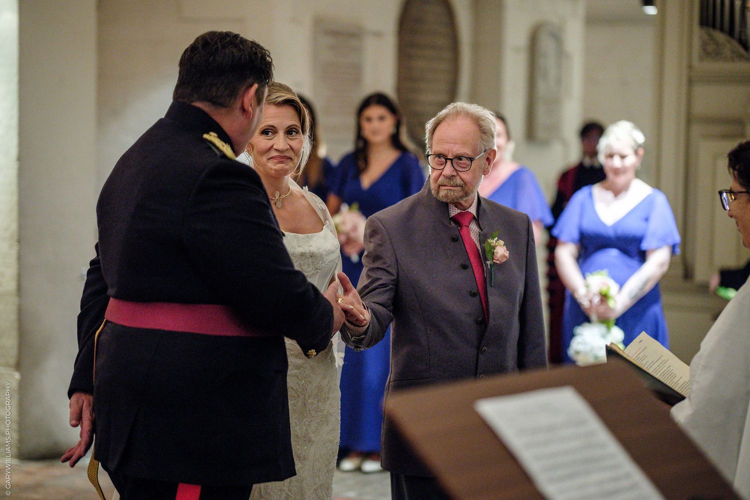 Wedding ceremony with guests in formal attire, groom shaking hands at the altar in an elegant venue.