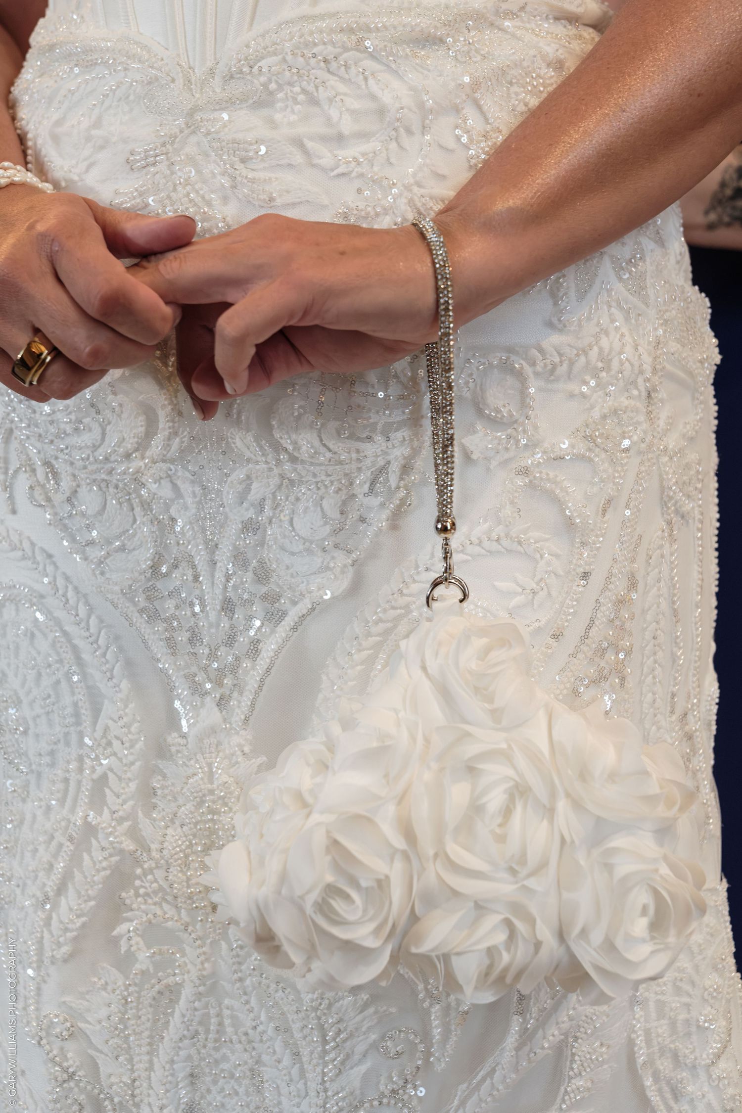 Bride in beaded white wedding gown holds elegant floral rose clutch purse with crystal chain strap.