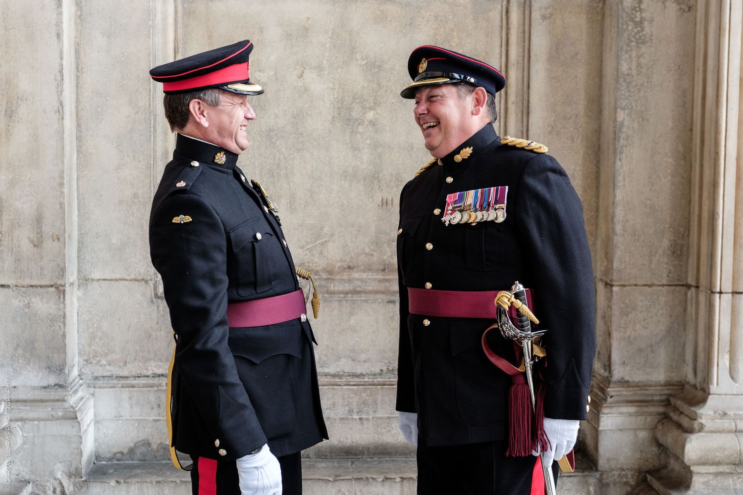 Two military officers in formal dress uniforms with medals converse outdoors at a ceremonial event.