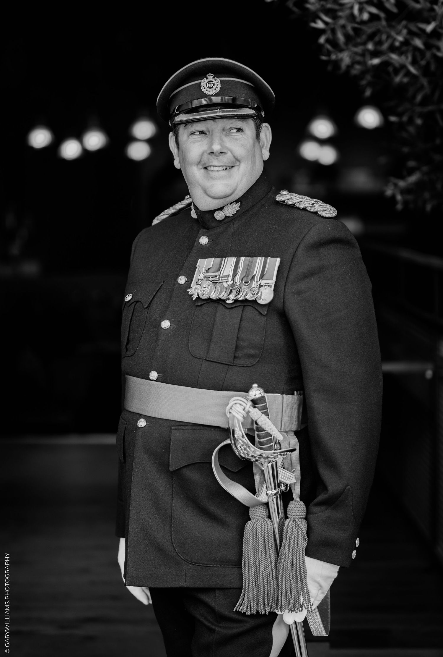 Black and white portrait of a smiling military officer in formal uniform with medals and ceremonial sword.
