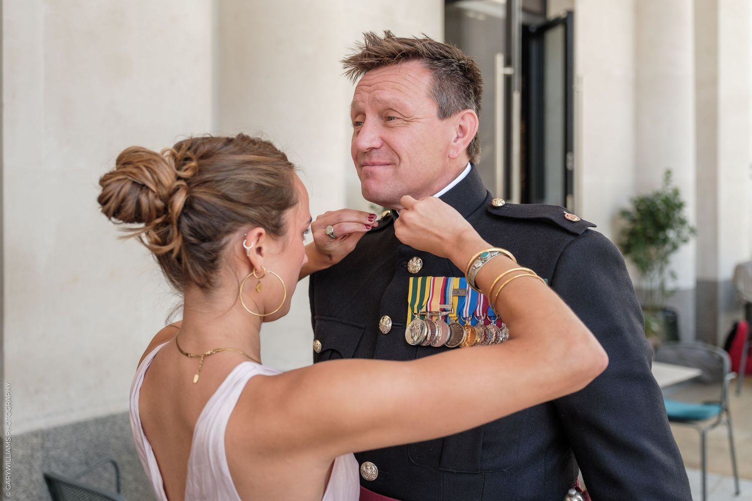 Woman pinning medals on a military officer in dress uniform at a formal outdoor ceremony.