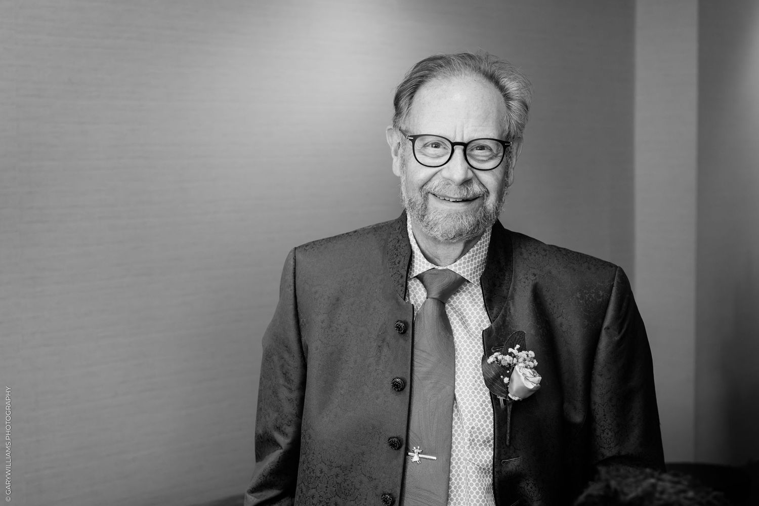 Black and white portrait of an elderly man wearing glasses, a suit, and a boutonniere, smiling warmly.
