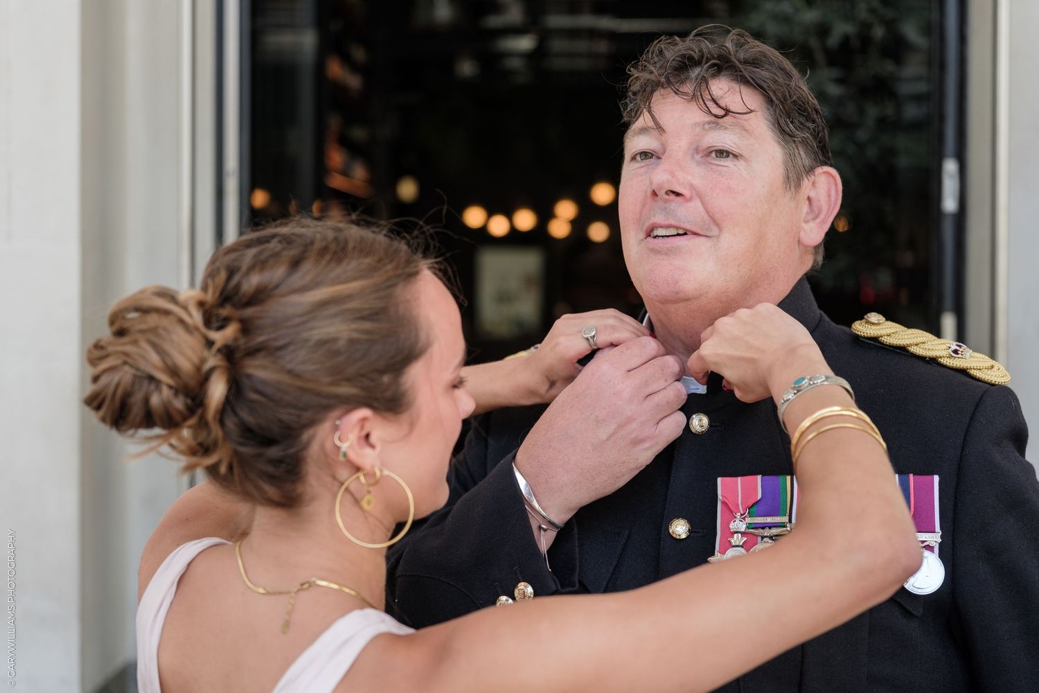 Woman adjusting military uniform medals on another persons jacket during an outdoor ceremony.