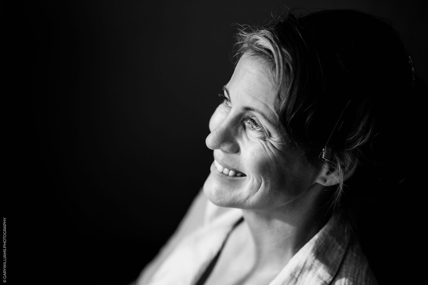 Black and white portrait of a smiling middle-aged woman looking upward against a dark background.