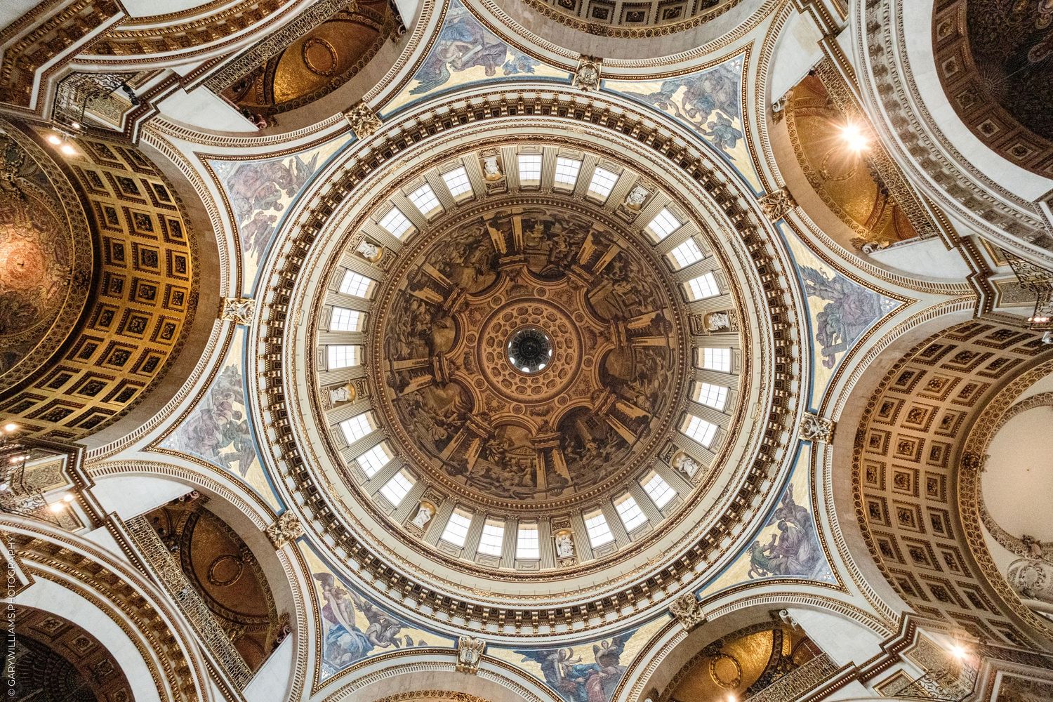 Ornate cathedral dome ceiling with golden mosaics, arched windows, and intricate baroque architectural details viewed from below.