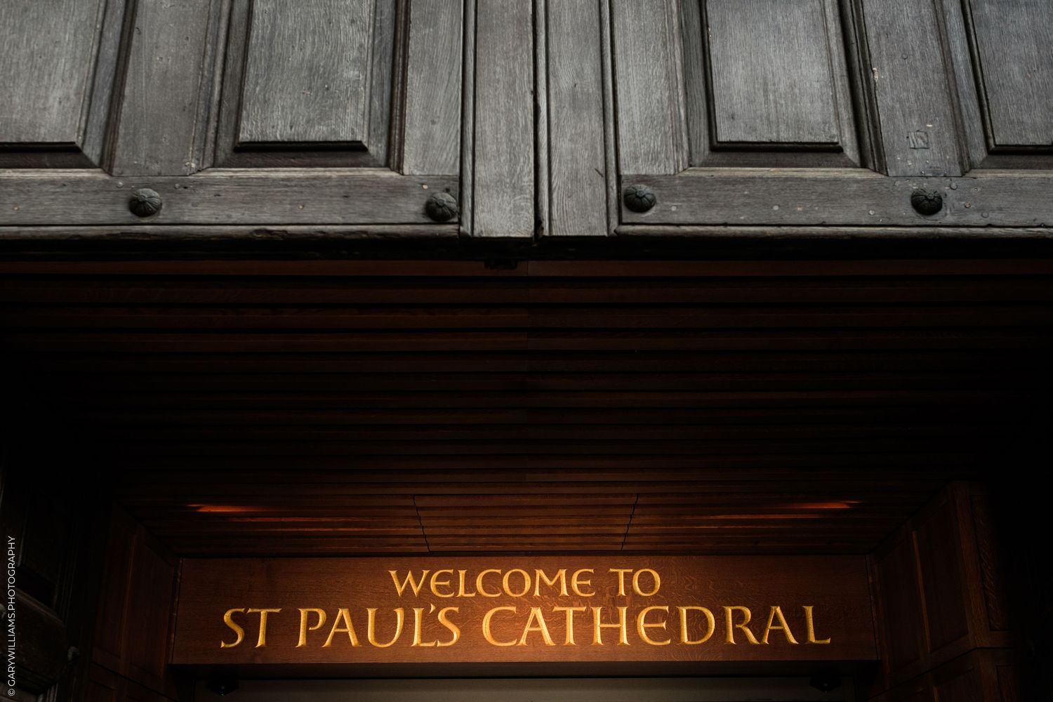 Illuminated welcome sign at the entrance of St Paul's Cathedral, London, beneath ornate wooden doors.