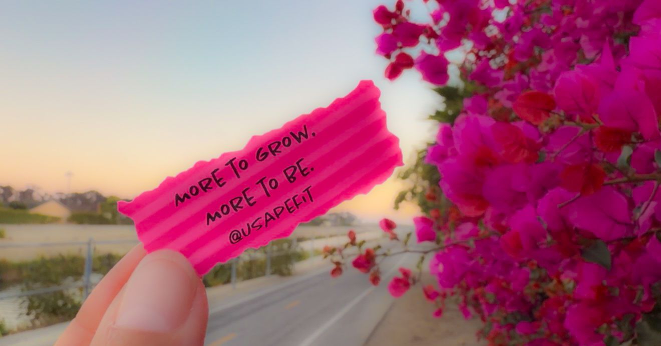 Hand holding pink paper with motivational quote, vibrant bougainvillea flowers, and scenic road at sunset.