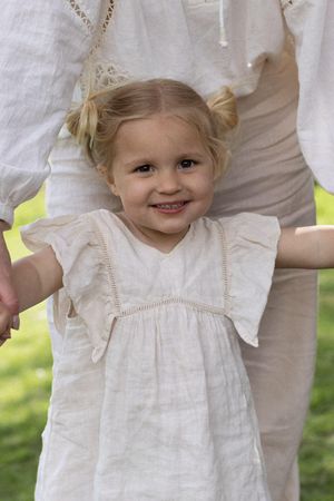 Smiling toddler girl in white ruffle dress stands outdoors holding hands with her mother during a mother a daughter photography session