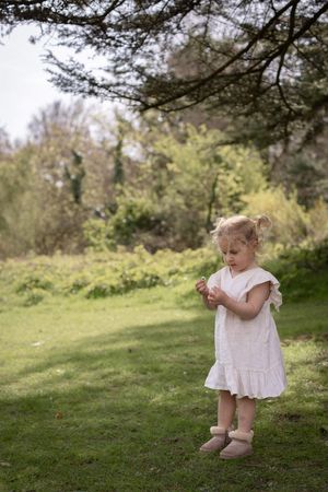 Toddler girl in white dress and boots standing on green grass in a park in Brighton