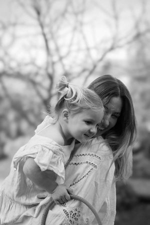 Black and white photo of a mother tenderly embracing her smiling toddler daughter outdoors during a family photography session in Brighton