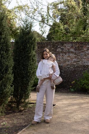 Woman in white blouse and linen trousers holding her daughter in a sunlit garden during a family photography session in Brighton