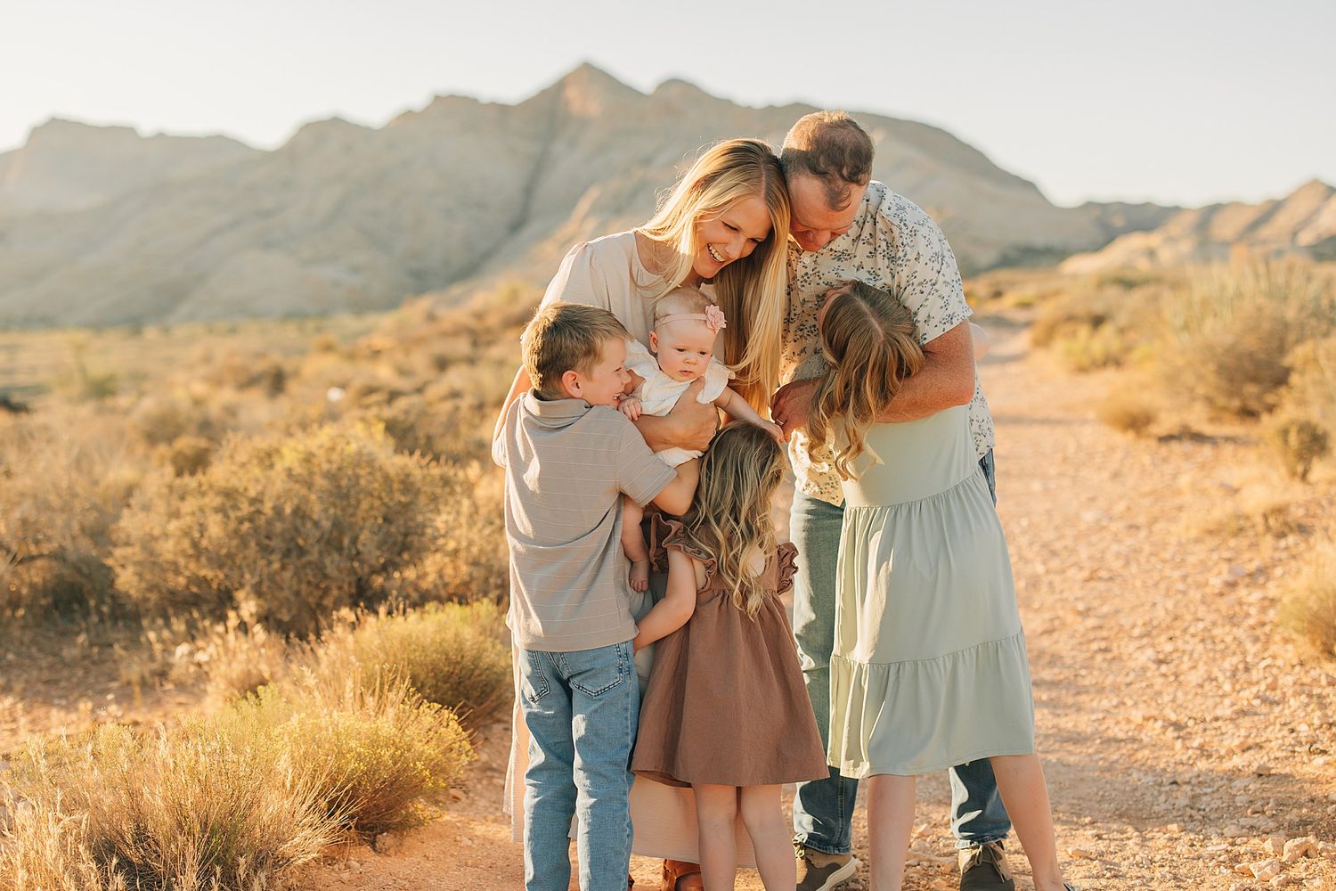 Family of five gathered on a desert path with mountain backdrop in warm golden light.