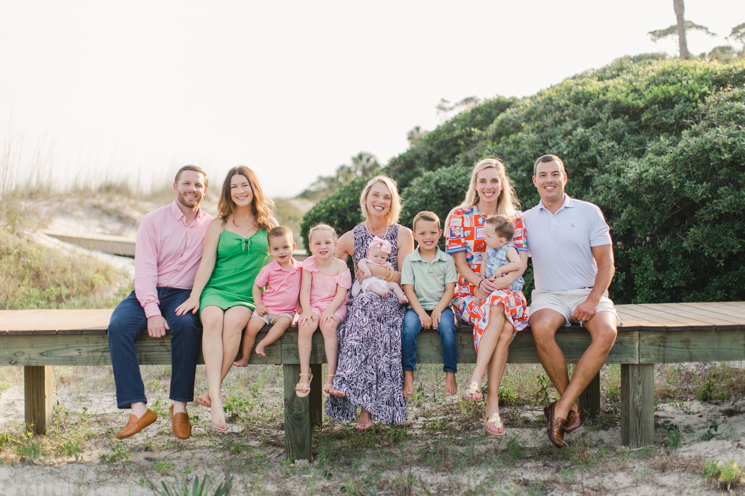 Sea Pines Beach photography with large family group smiling together on a wooden bench at a sunny beach with sand dunes and greenery.