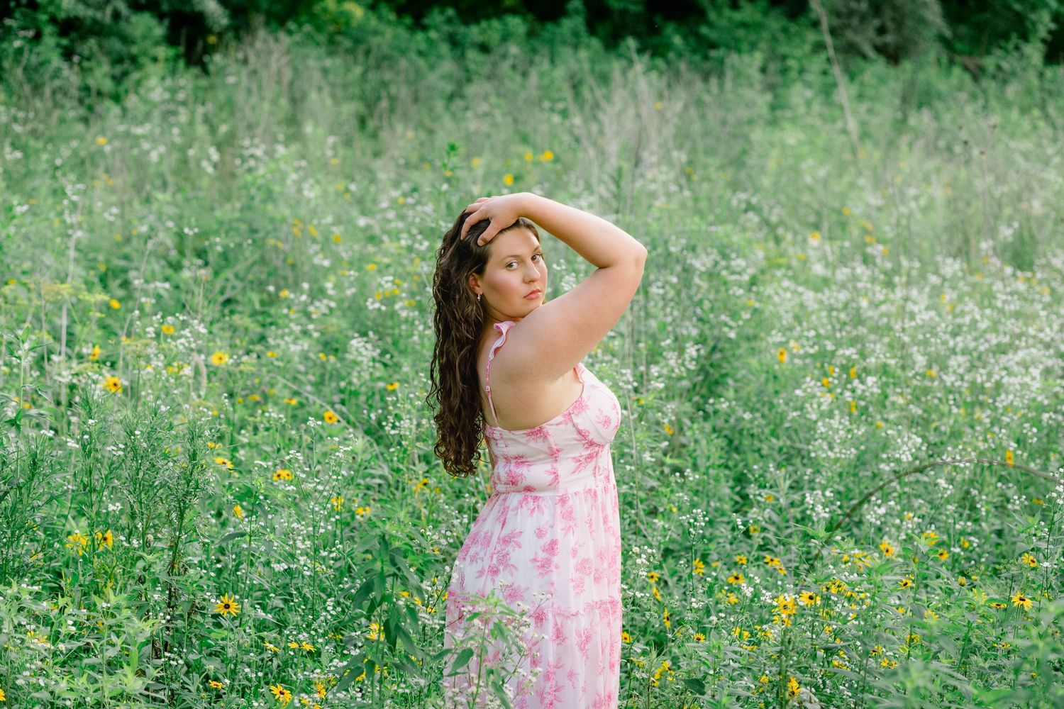 Young blonde woman in white lace dress smiling in a vibrant yellow wildflower meadow on a sunny day.