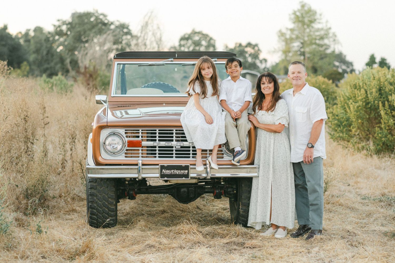 Family of four posing in front of a vintage Ford Bronco in a golden field during a professional photo session.