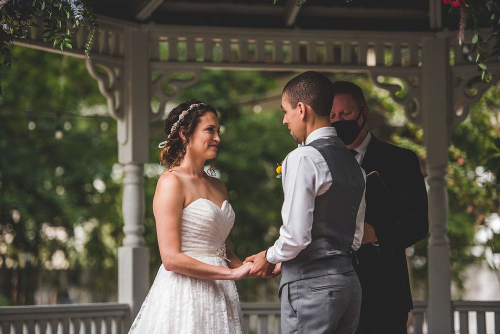 Bride and groom exchange vows holding hands under elegant gazebo with officiant.