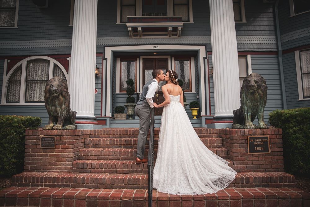 Bride and groom share a kiss on brick steps outside a historic mansion with lion statues.
