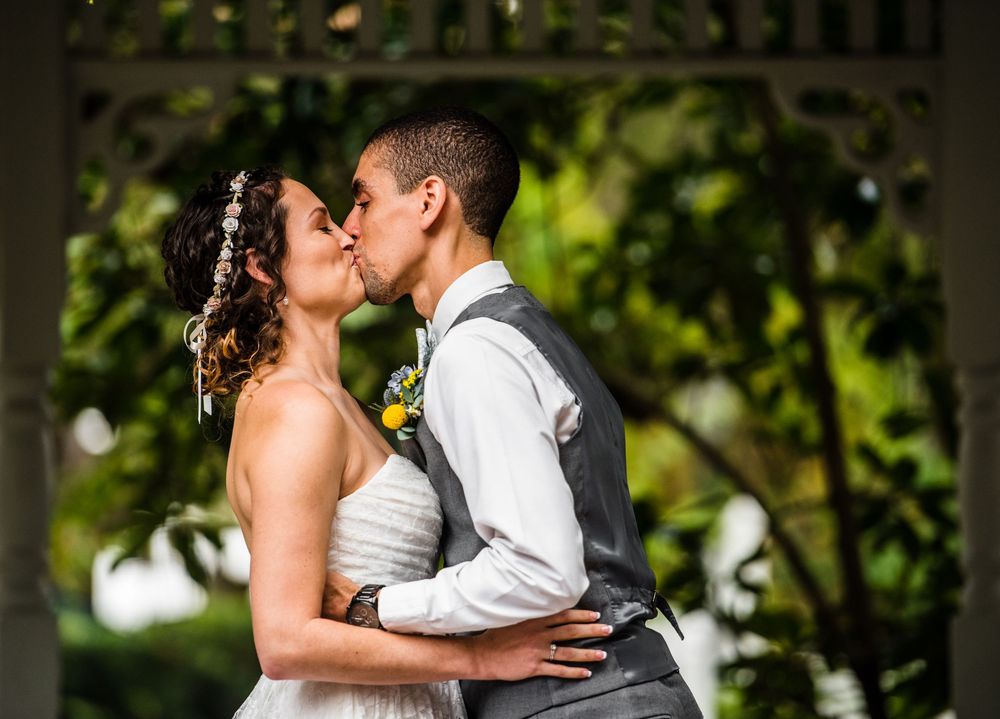 Newlyweds share a romantic kiss under a garden gazebo on their wedding day.