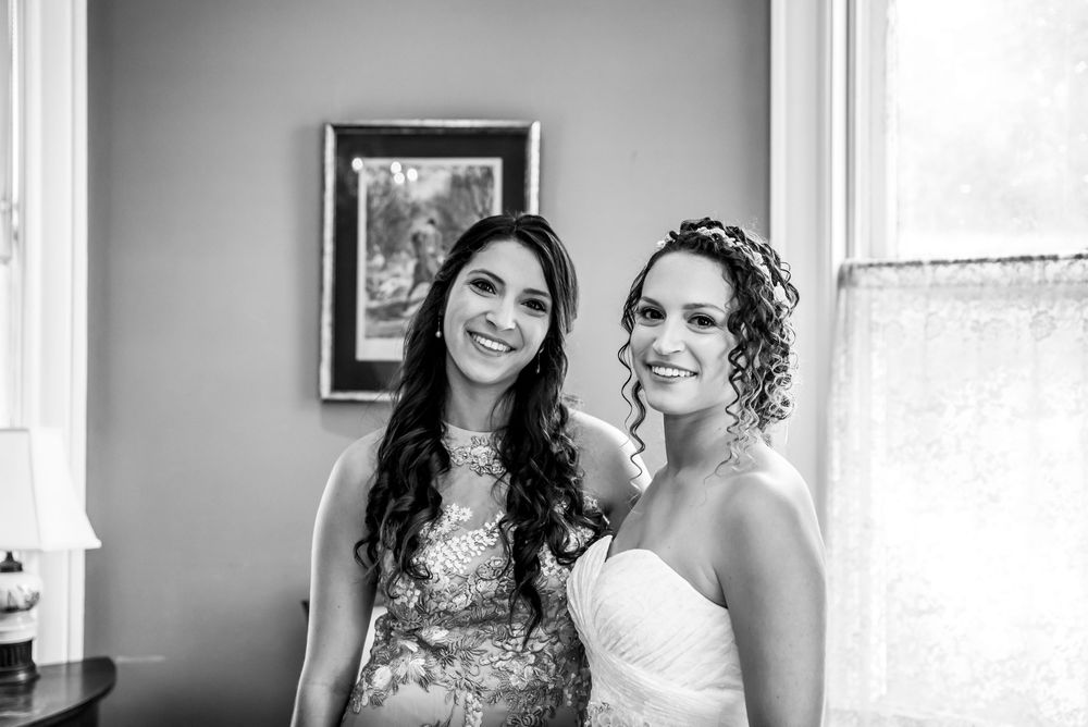 Black and white portrait of smiling bride and bridesmaid posing together near window before wedding.