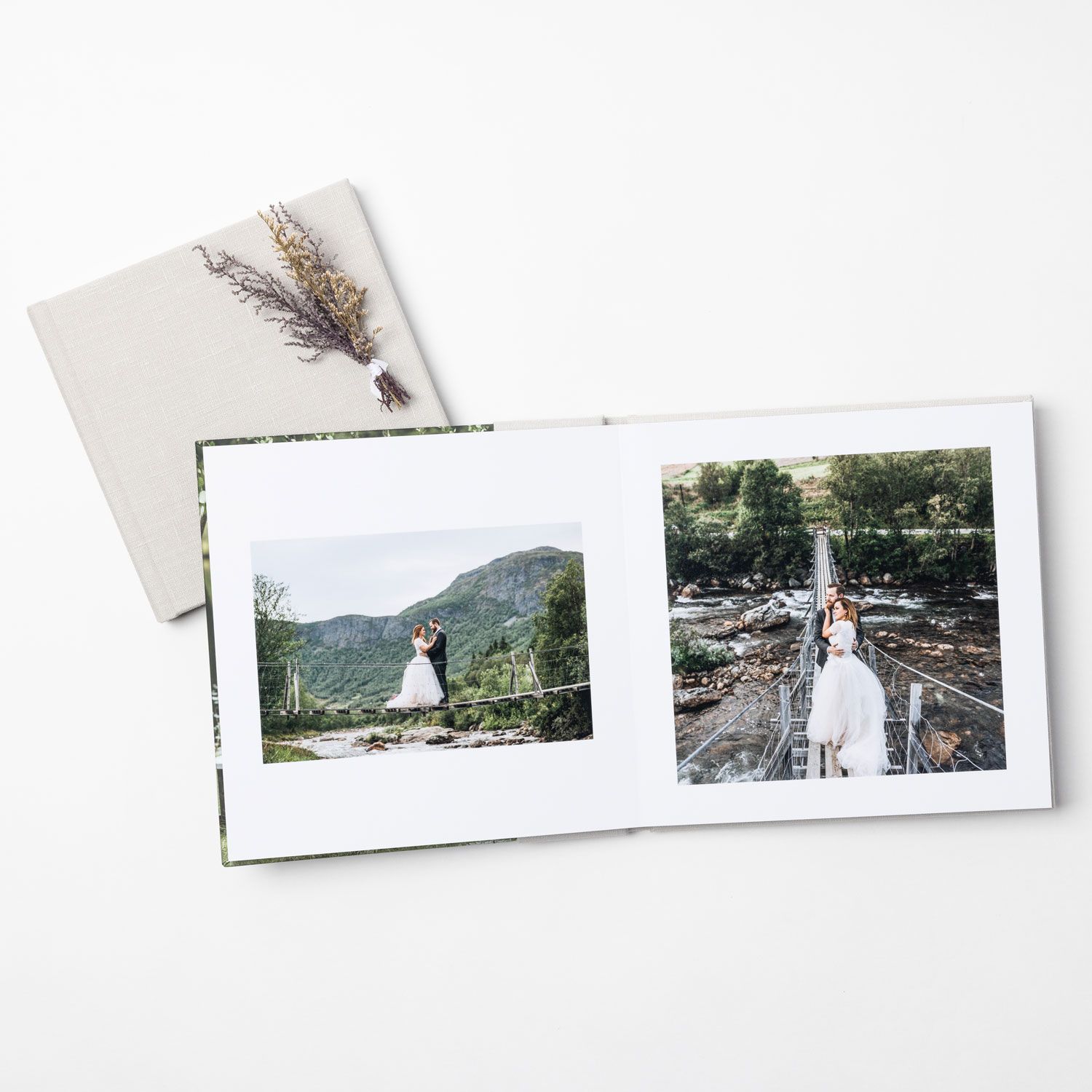 An open wedding photo album displaying two landscape photos of a couple, with a floral sprig on the cover.