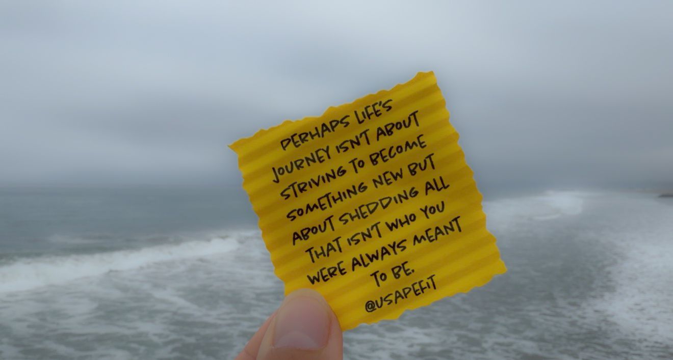 Hand holding yellow note with life journey quote against stormy ocean background.