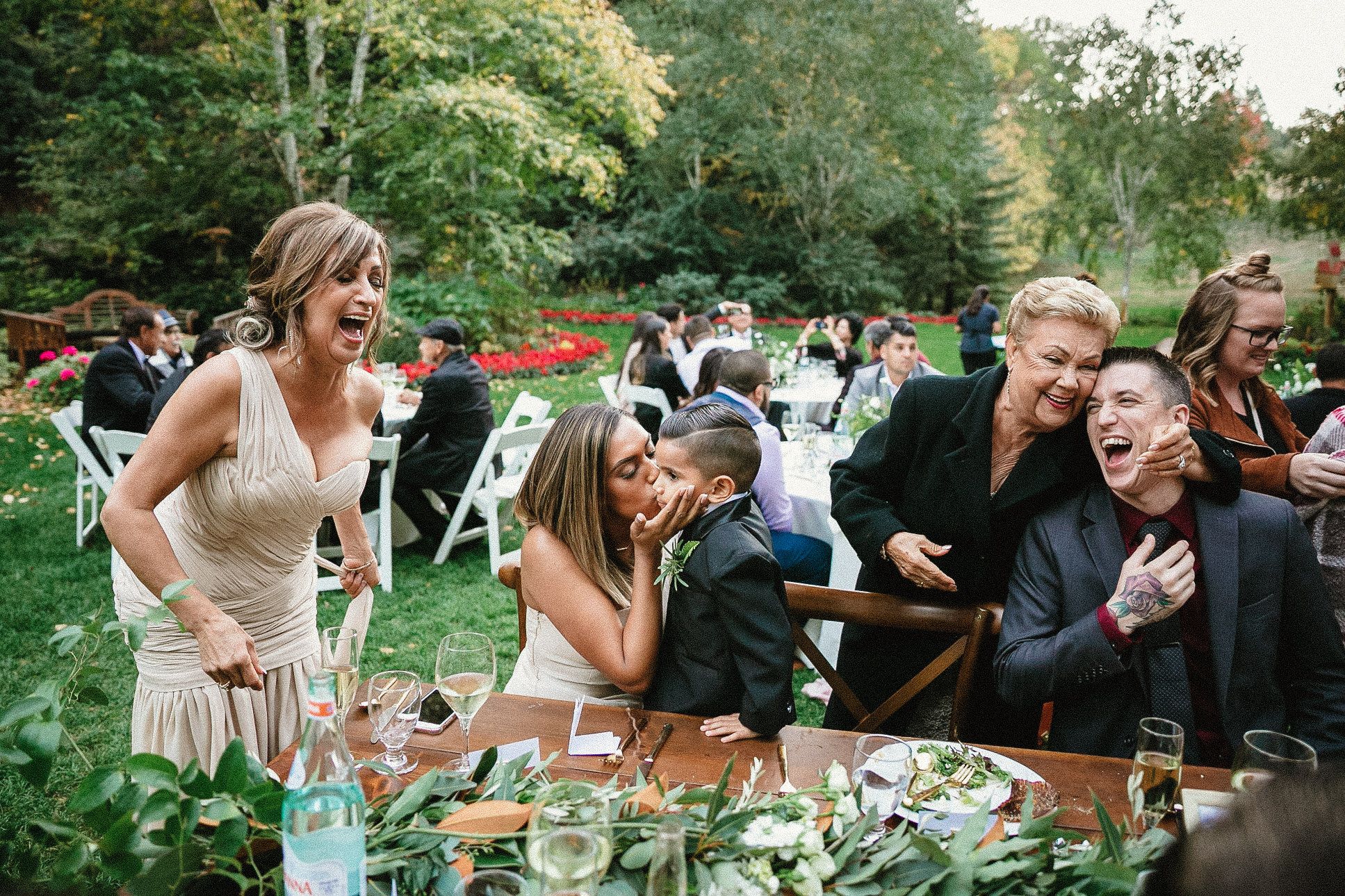 Guests laughing and celebrating at an outdoor wedding reception surrounded by lush greenery and festive tables.