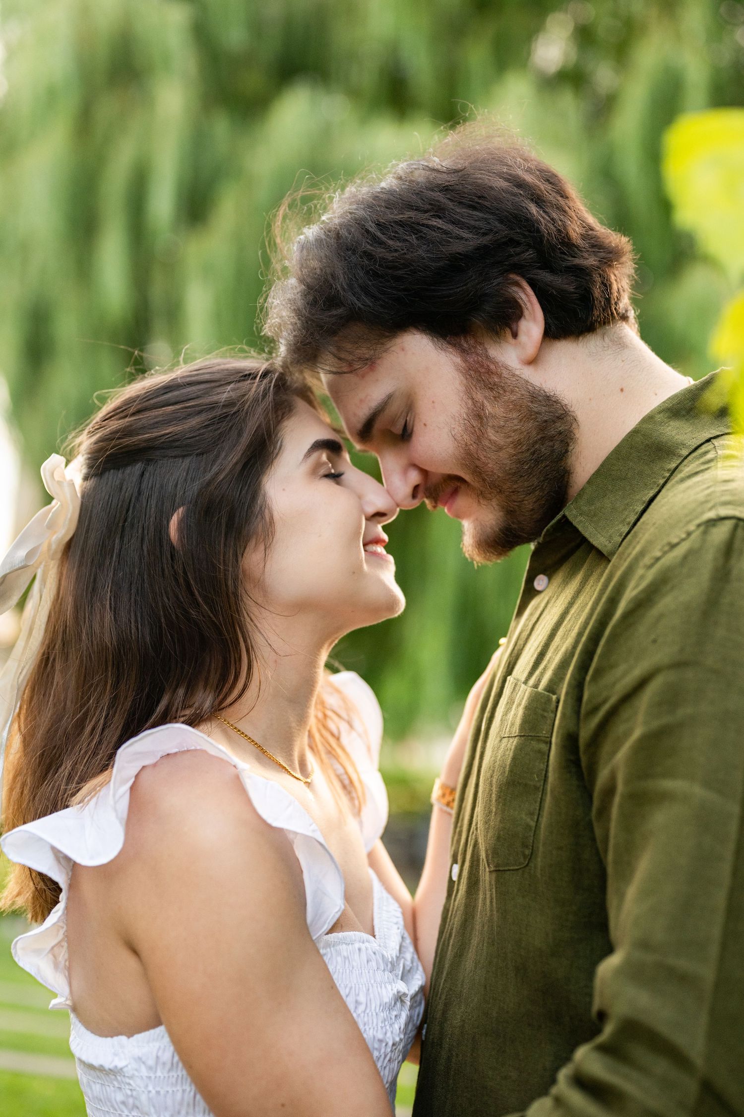 Romantic couple sharing a tender moment about to kiss in a lush green park on a sunny day.