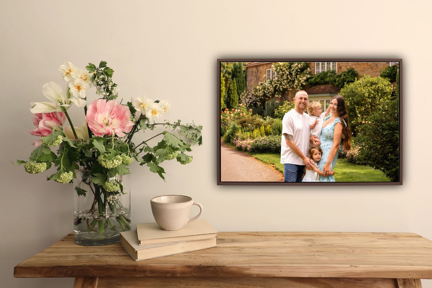 Framed family portrait photo displayed on a rustic wooden shelf beside a vase of pink flowers and a white coffee mug.