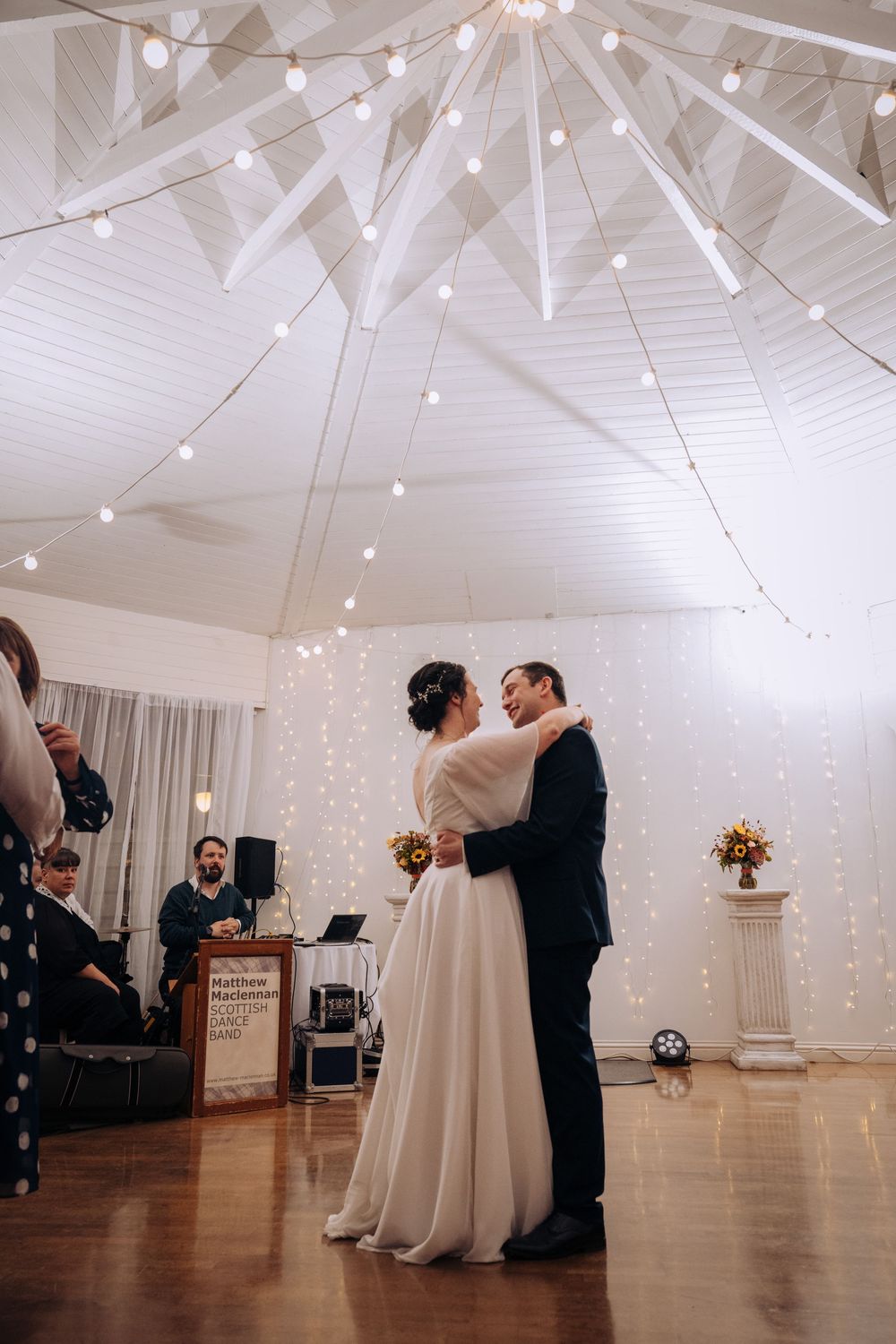 Bride and groom share their first dance under string lights in an elegant white tent wedding venue.