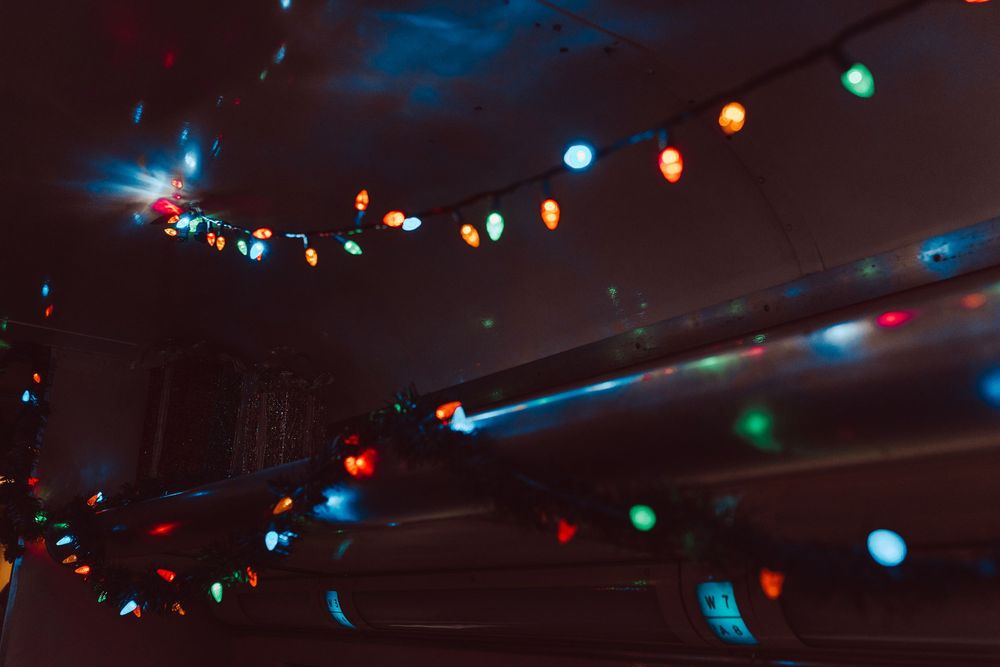 Colorful Christmas string lights glowing in red, green, and blue against a dark ceiling in a dimly lit room.