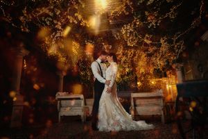 Romantic wedding couple embracing under glowing fairy lights in a warmly lit outdoor garden at night.