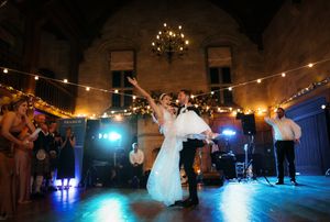 Bride and groom share first dance at elegant wedding reception with string lights and live band in historic venue.