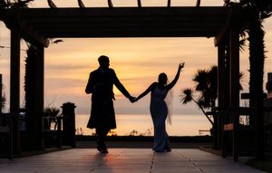 Silhouette of a couple holding hands at sunset under a pergola with ocean views, perfect for a romantic wedding photo.