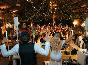 Bride and groom celebrate with guests on a packed dance floor at an elegant wedding reception with string lights.