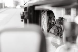 Black and white photo of a smiling blonde woman reflected in a car mirror holding flowers.