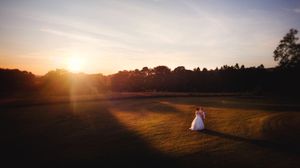 Bride and groom embracing at sunset on a lush green field with warm golden light and tree silhouettes.