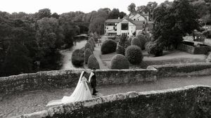 Black and white wedding photo of bride and groom on stone terrace overlooking manicured gardens and elegant country estate.