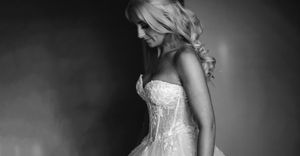 Black and white photo of a blonde woman in an elegant strapless wedding gown posing gracefully in a studio.