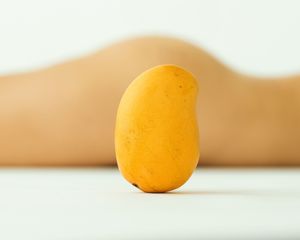 A ripe yellow mango standing upright on a white surface with a soft blurred background.