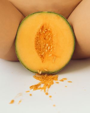 Halved cantaloupe melon showing vibrant orange flesh and seeds on a white surface.