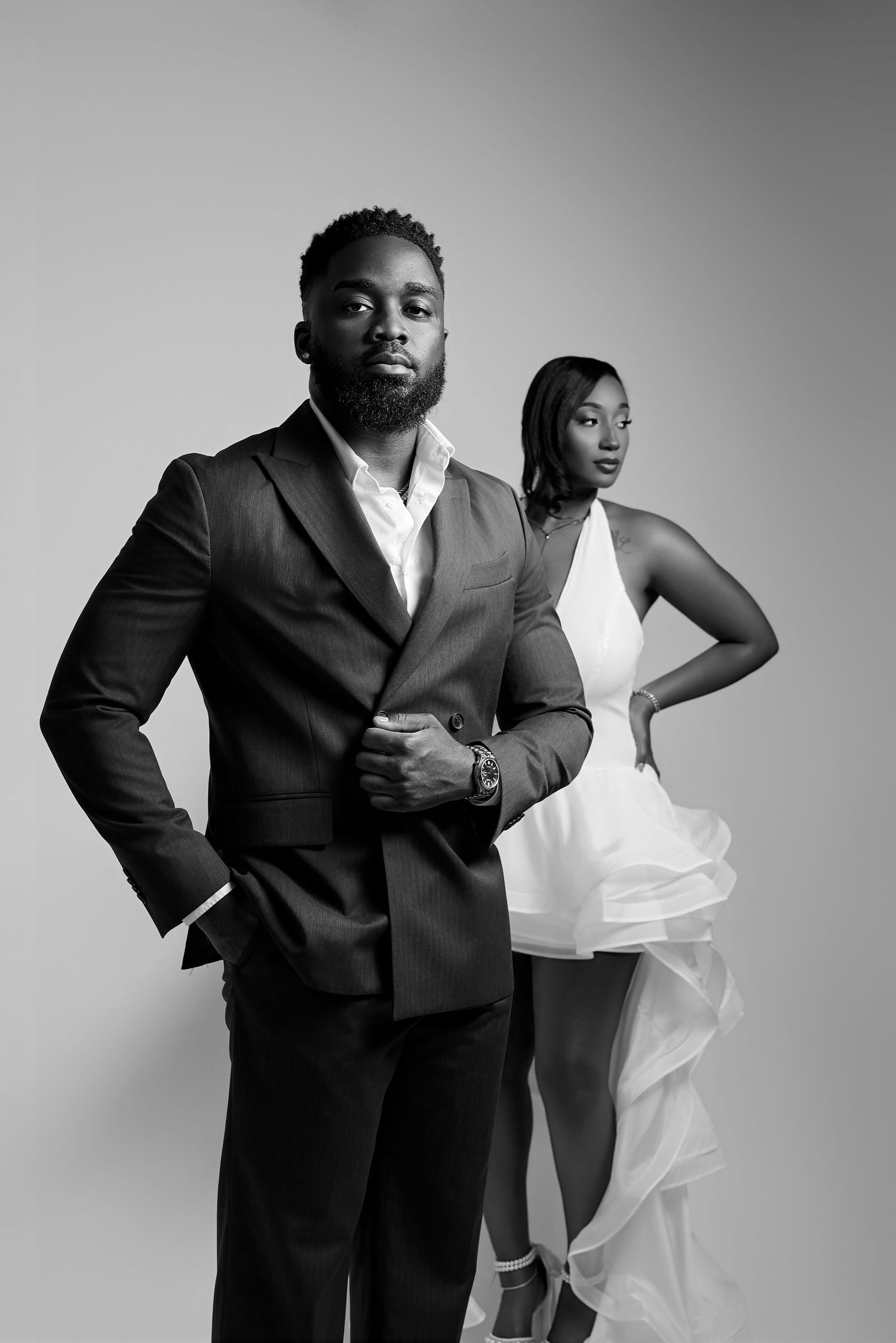 Black and white photo of an elegant couple, man in suit and woman in white dress, posing in a studio.