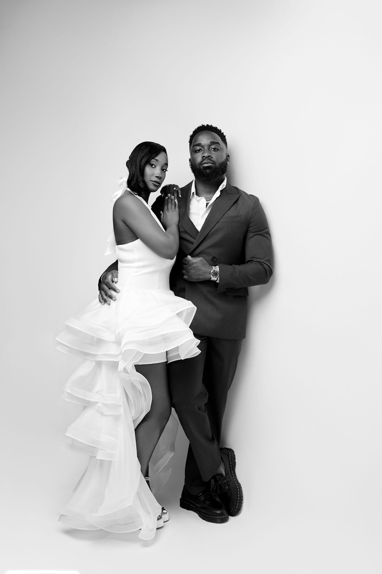 Black and white photo of a couple in wedding attire, woman in ruffled dress, man in suit, posing elegantly.