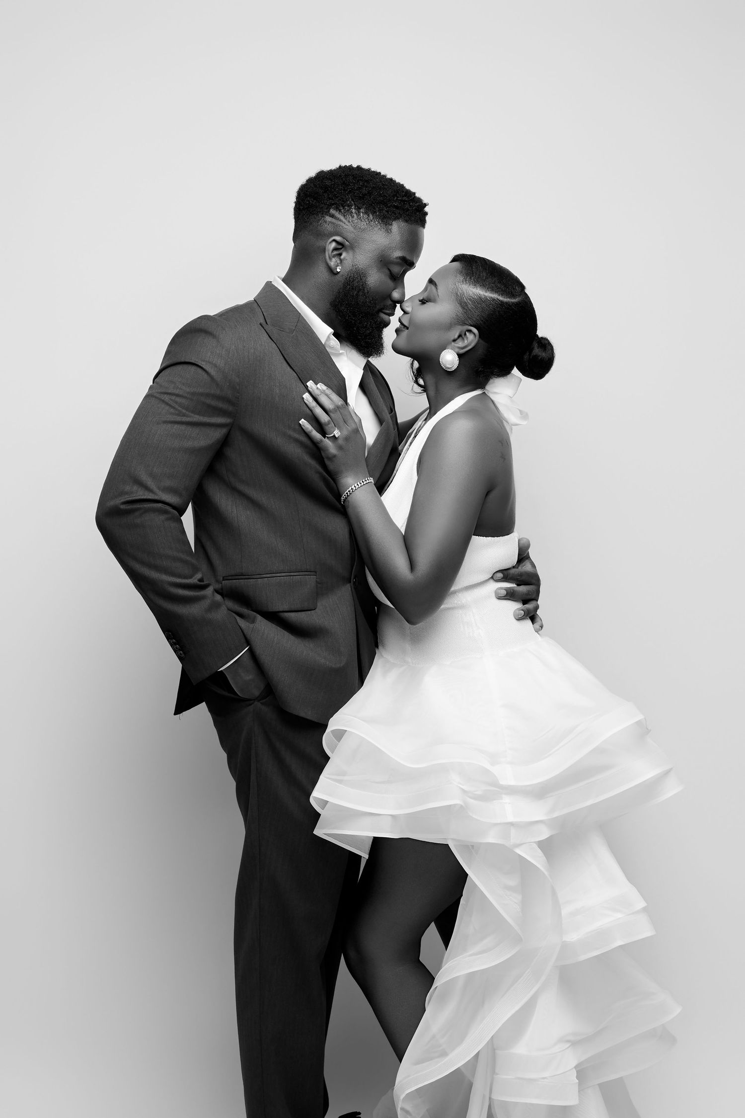 Elegant black and white photo of a couple kissing, man in suit and woman in ruffled white dress.