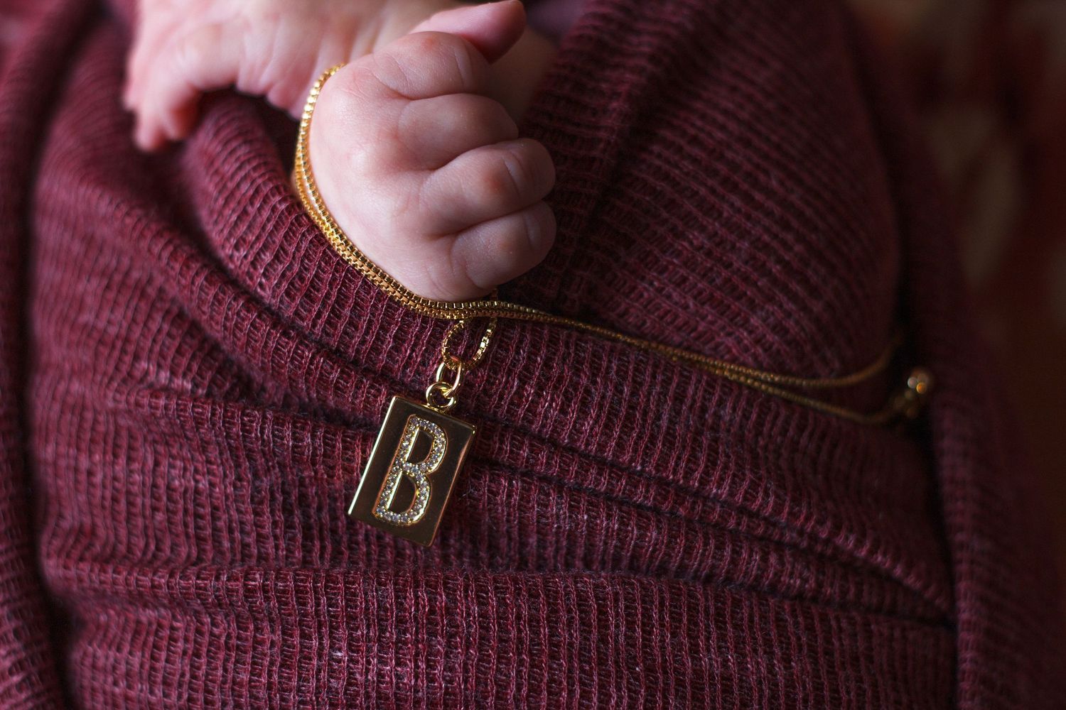 Burgundy newborn wrap sample for baby photography sessions with newborns hands shown clutching a necklace.
