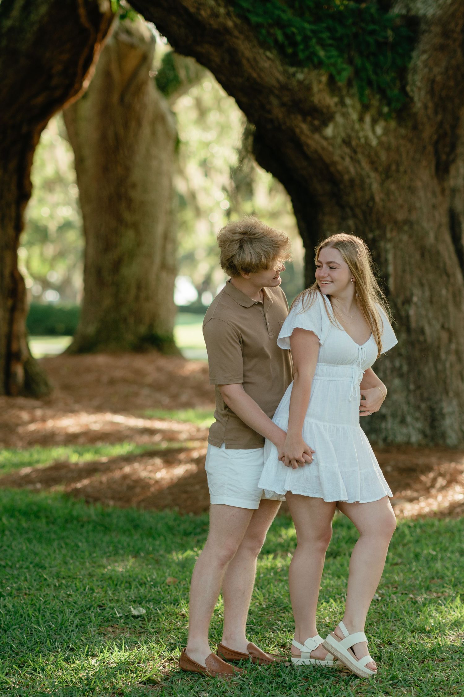 Avenue of the oaks engagement proposal session, young couple smiling at one another by oak trees on St. Simons Island